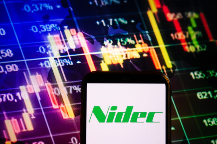 Smartphone displaying logo of Nidec company on stock exchange diagram background